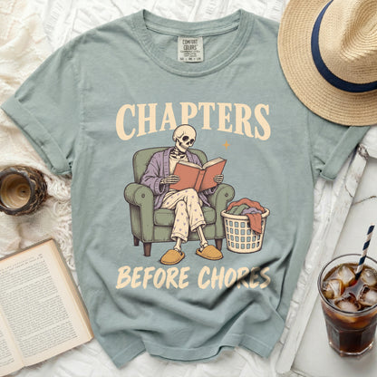 Skeleton reading in chair with laundry basket, text "Chapters Before Chores".