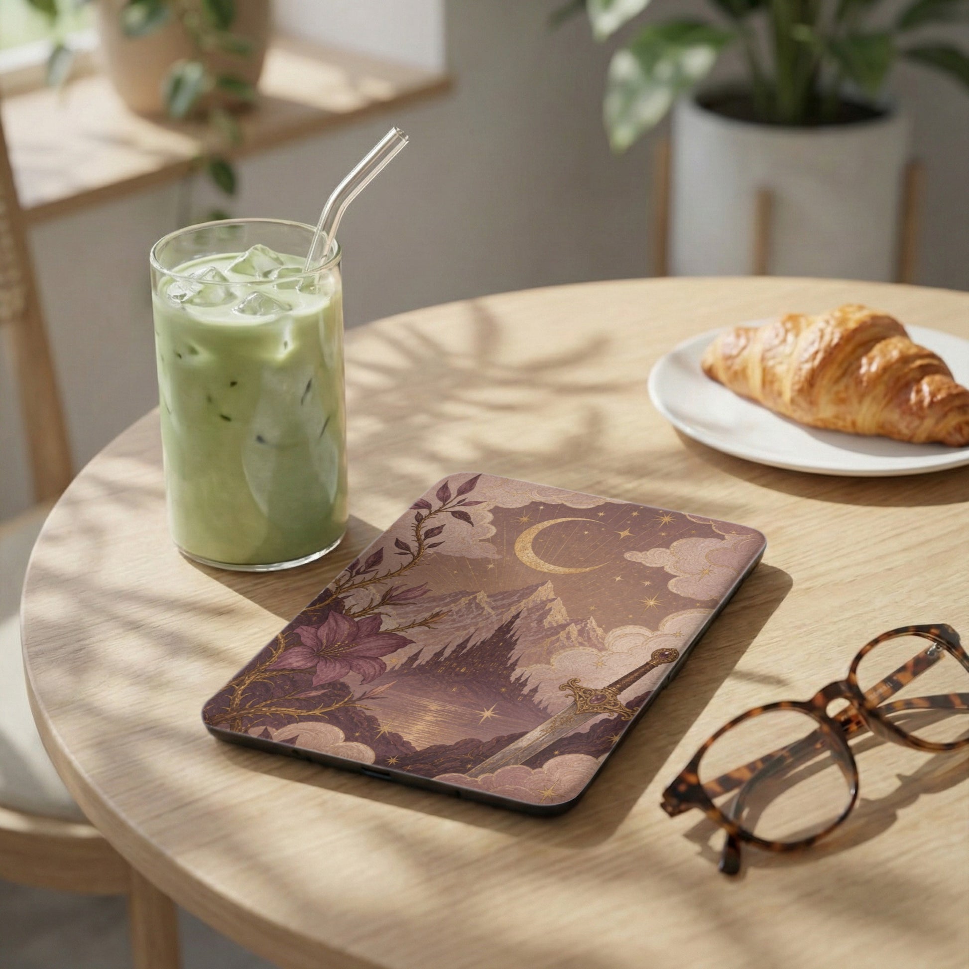 Device case with fantasy art design, featuring sword and moon, on a table.