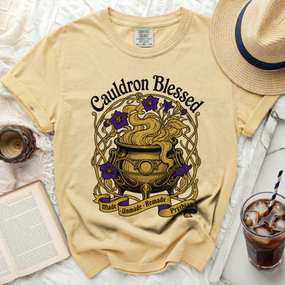 Yellow t-shirt with a "Cauldron Blessed" graphic featuring a cauldron and purple flowers.