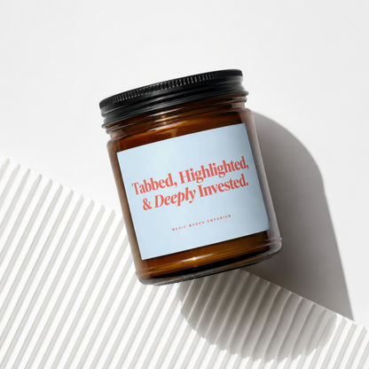 Amber glass candle with label reading "Tabbed, Highlighted, & Deeply Invested."