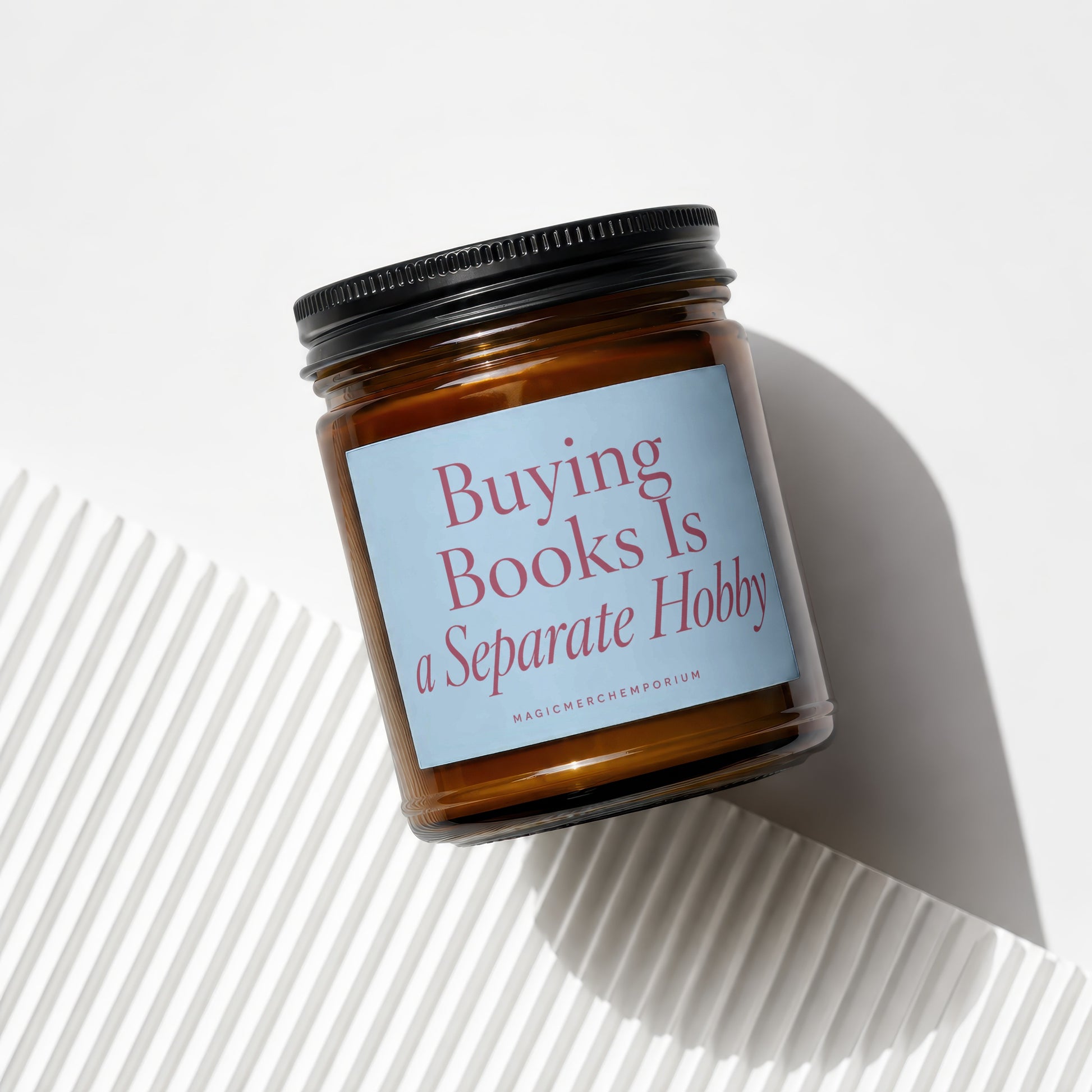 Amber jar candle with light blue label reading "Buying Books Is a Separate Hobby"