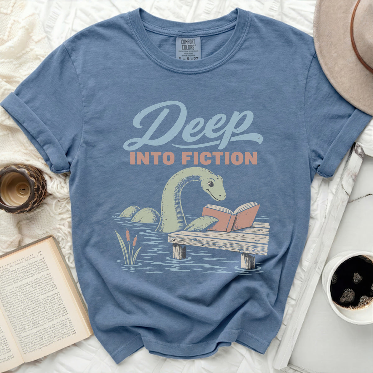 T-shirt with a graphic of a Loch Ness Monster reading a book that says "Deep Into Fiction".