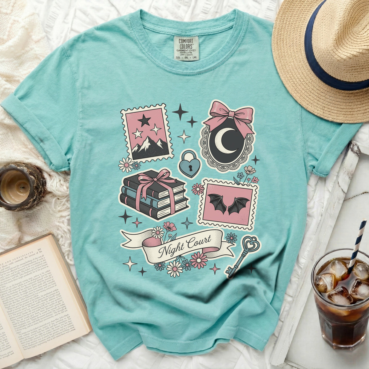 Teal t-shirt with "Night Court" banner, books, bats, and celestial motifs.