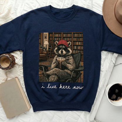 Navy sweatshirt with graphic of raccoon in armchair and text "i live here now."