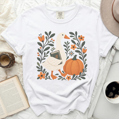 White t-shirt with a goose holding a book surrounded by pumpkins and flowers.