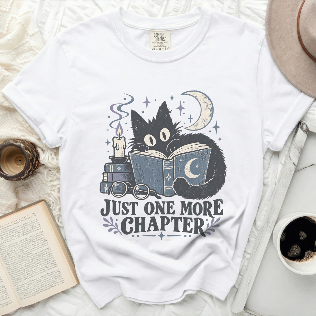 White t-shirt with a black cat reading a book, moon, candle, and text "JUST ONE MORE CHAPTER".