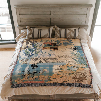 a bed with a decorative blanket on it. The blanket features various floral and nature-inspired designs, including a woman holding a book, flowers, and a butterfly. The blanket is spread over the bed, covering the mattress and pillows.
