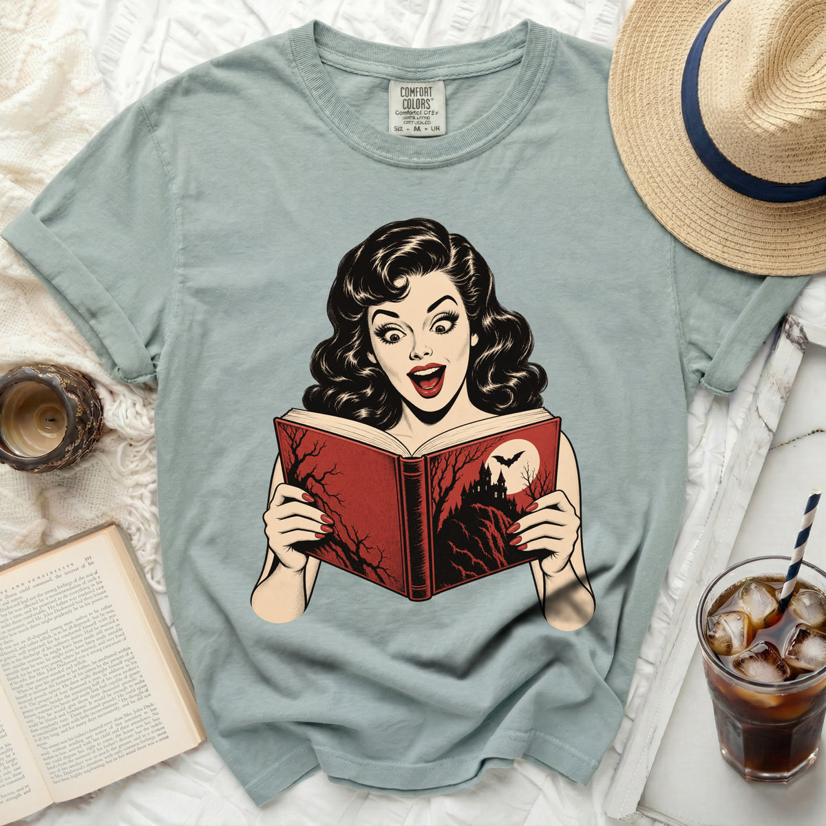 Comic style woman reads spooky book with bat and castle on teal t-shirt.