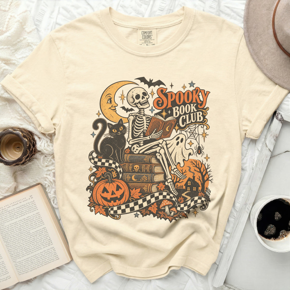 Skeleton reading a book with "Spooky Book Club" text, black cat, pumpkin, and moon.