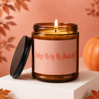 Amber candle with lit wick, label reads "Judge Me by My Bookshelf".