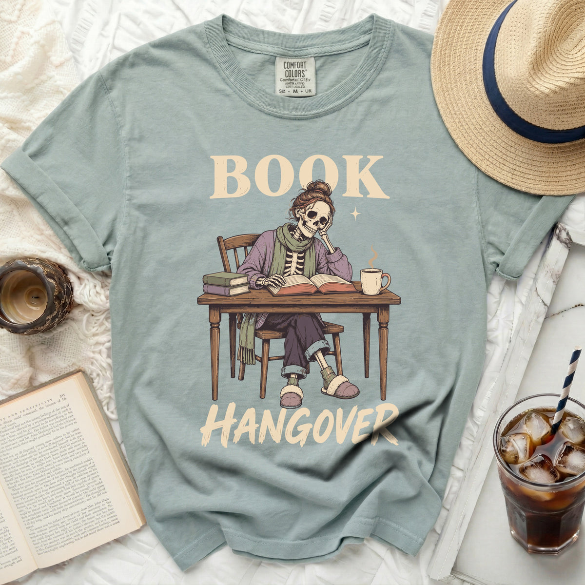 Skeleton reading at a desk with text "BOOK HANGOVER" on a t-shirt.