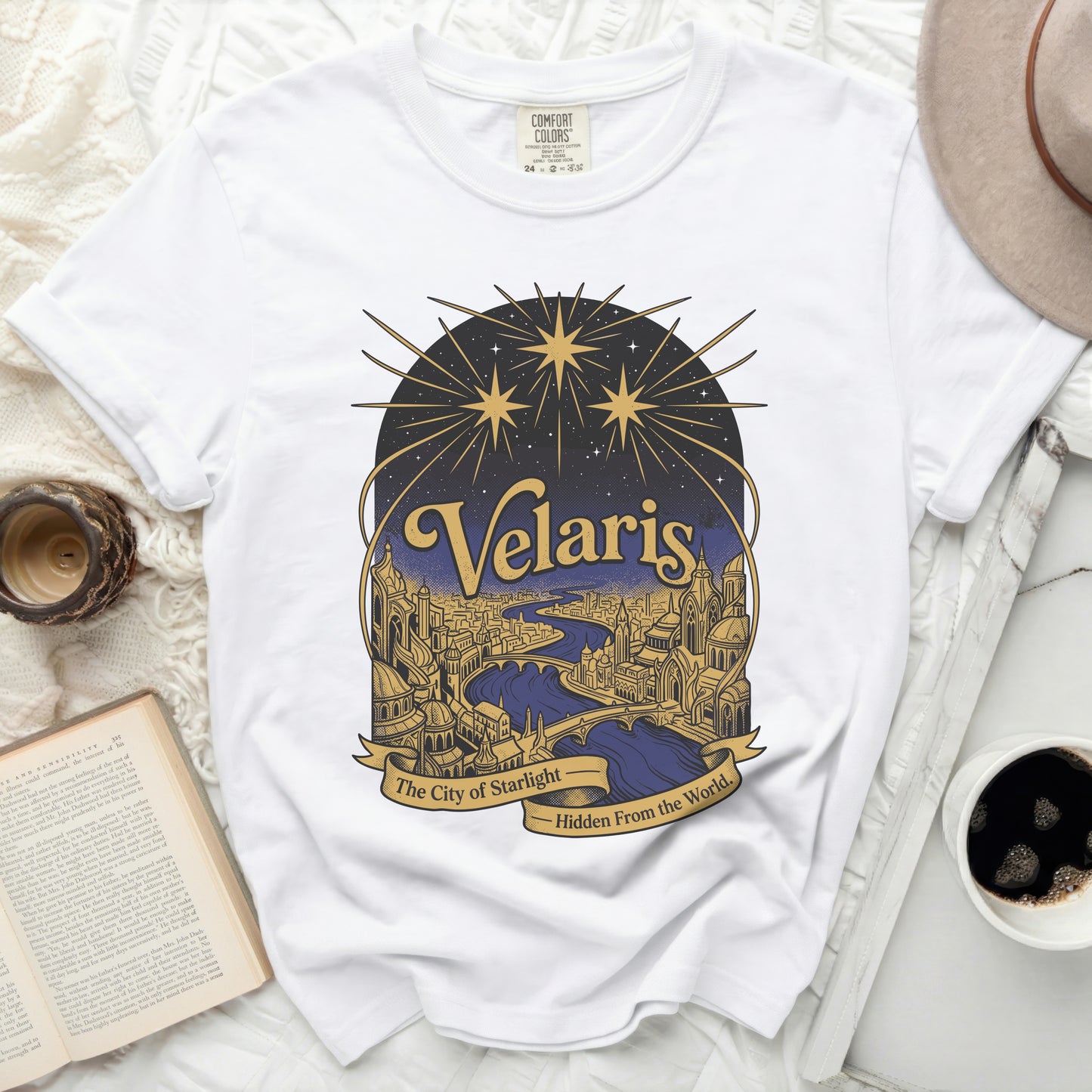 White t-shirt with gold and blue graphic of a city under starry skies.
