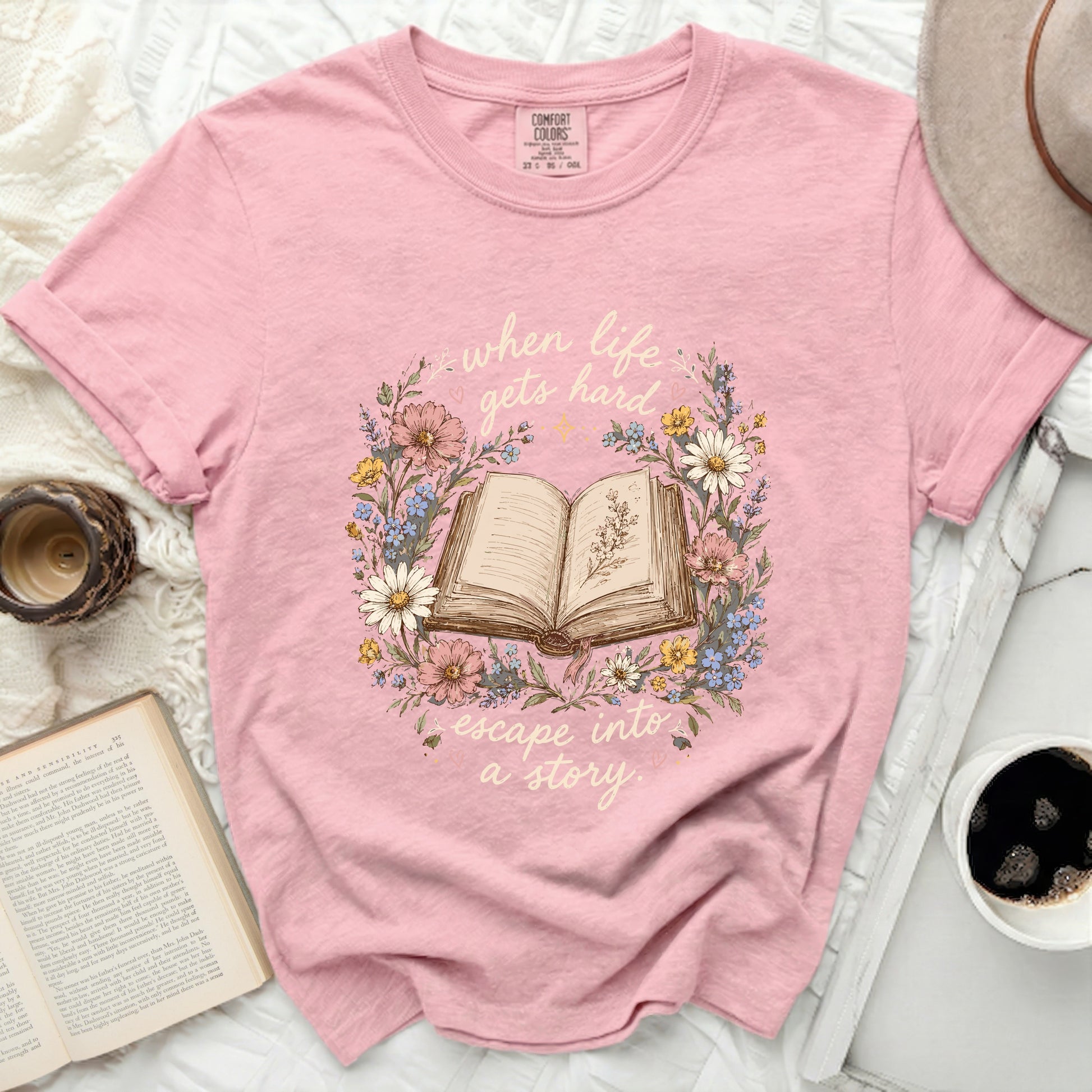 Pink t-shirt with open book surrounded by floral wreath and text.