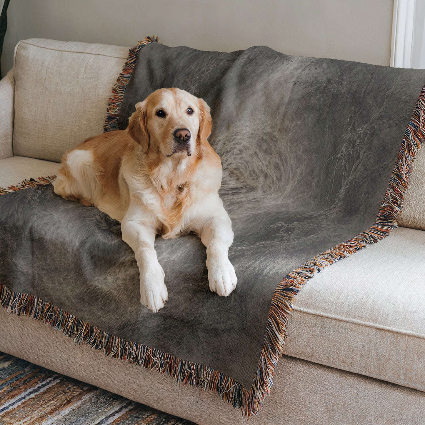A golden retriever dog is lying on a gray blanket on a beige couch, looking directly at the camera.