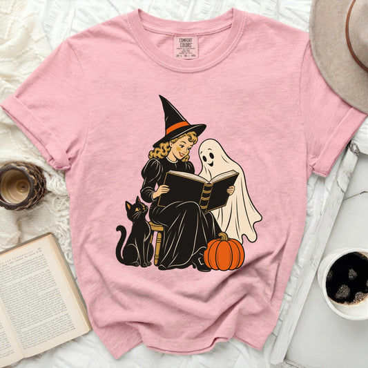 Pink t-shirt with graphic of a witch reading to a ghost, with cat and pumpkin.