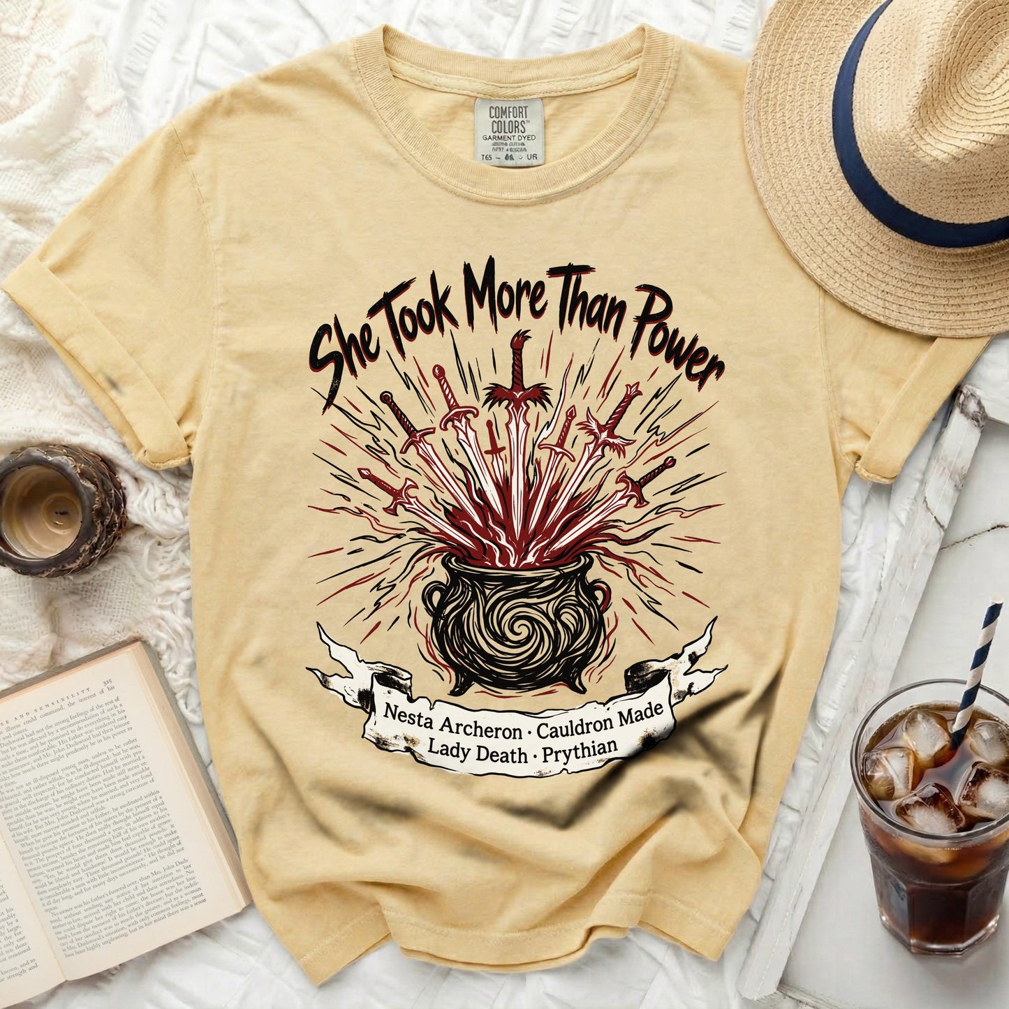 Yellow t-shirt with "She Took More Than Power" and swords in cauldron graphic.