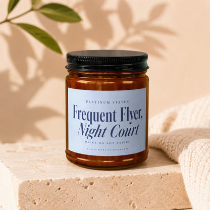 Amber glass candle jar with a black lid and blue label resting on a stone surface.