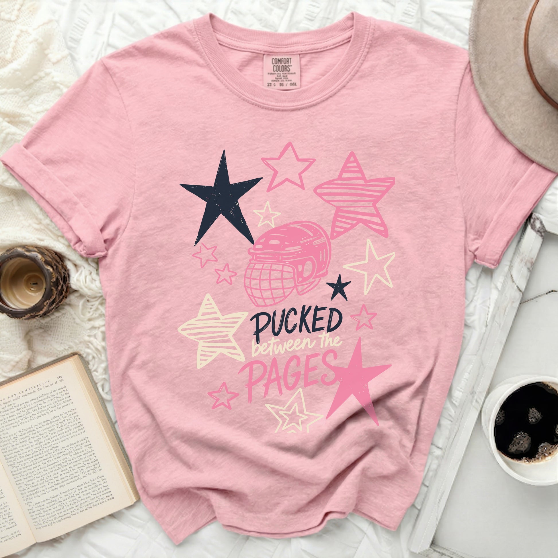 Pink Comfort Colors t-shirt with hockey helmet and stars, "Pucked Between the Pages" text.