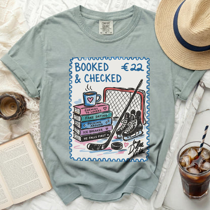 T-shirt with stamp graphic: "BOOKED €22 & CHECKED" and book titles.
