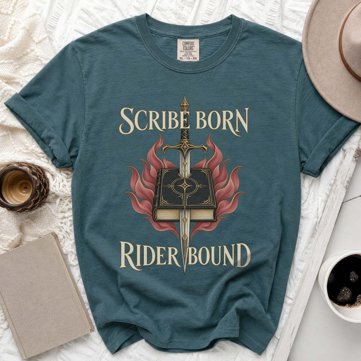 A dark blue t-shirt displays the text "SCRIBE BORN RIDER BOUND" with a book, sword, and flames graphic.