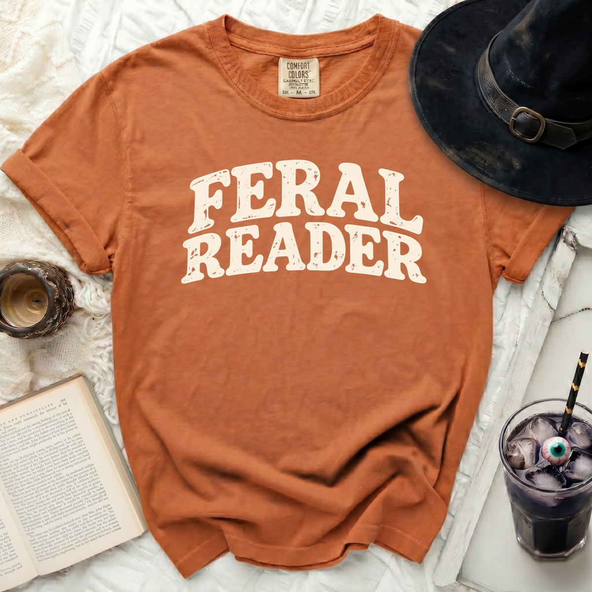 Orange t-shirt with cream "FERAL READER" graphic and a black witch hat.