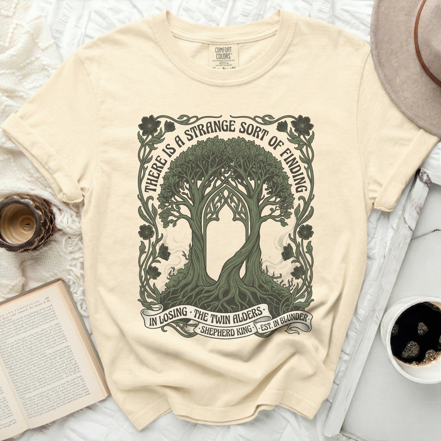 T-shirt with twin alder trees and quote "There is a strange sort of finding".