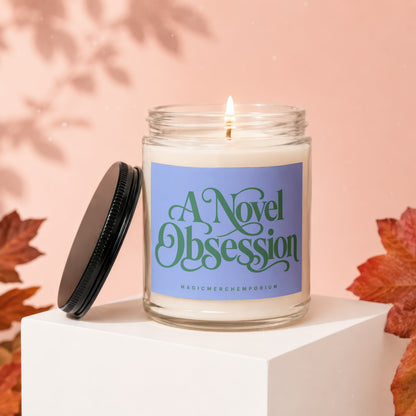 Lit glass candle with purple label reading "A Novel Obsession" and "MAGICMERCHEMPORIUM".
