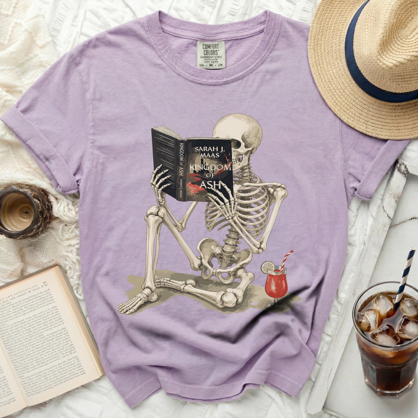 Skeleton reading "Kingdom of Ash" by Sarah J. Maas book with a drink.