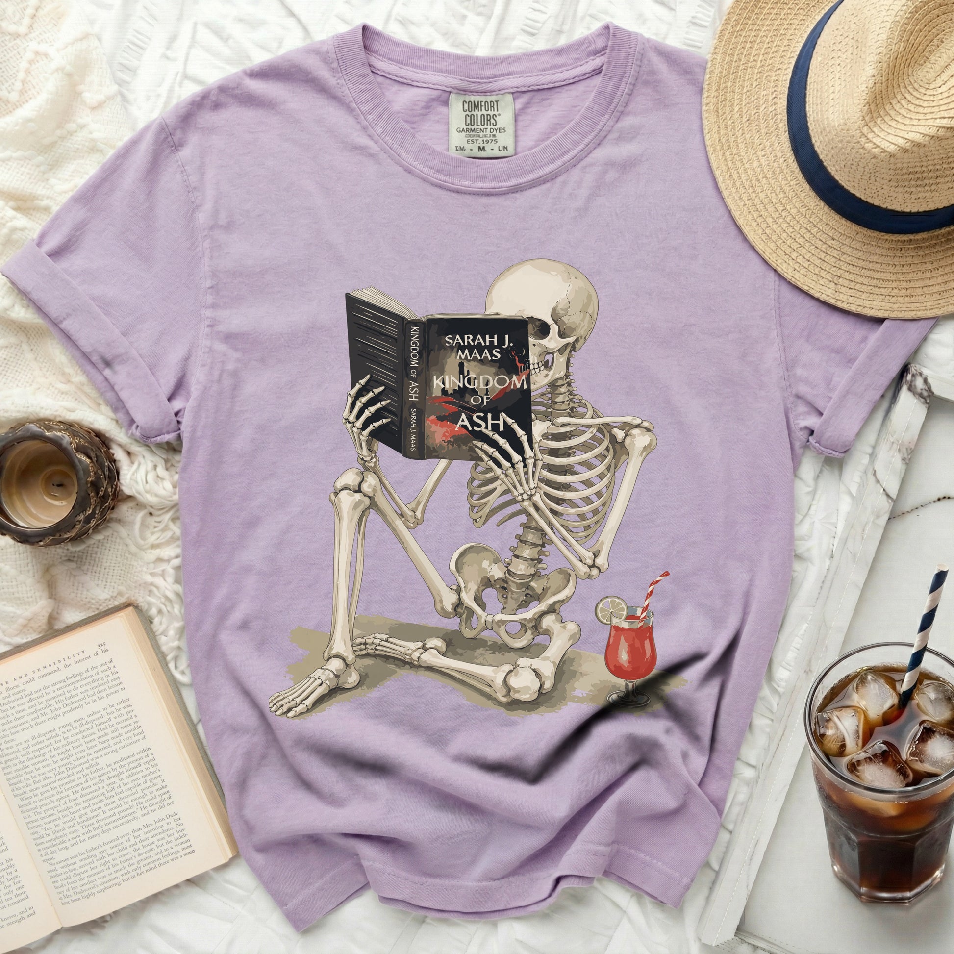 Skeleton reading "Kingdom of Ash" by Sarah J. Maas book with a drink.