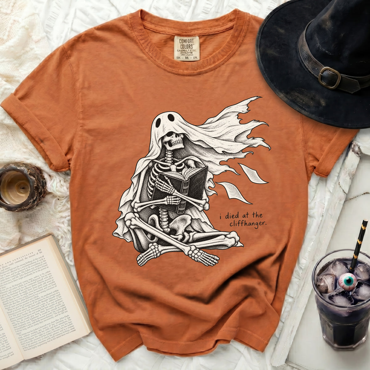 Skeleton in ghost costume reading a book with text "i died at the cliffhanger."