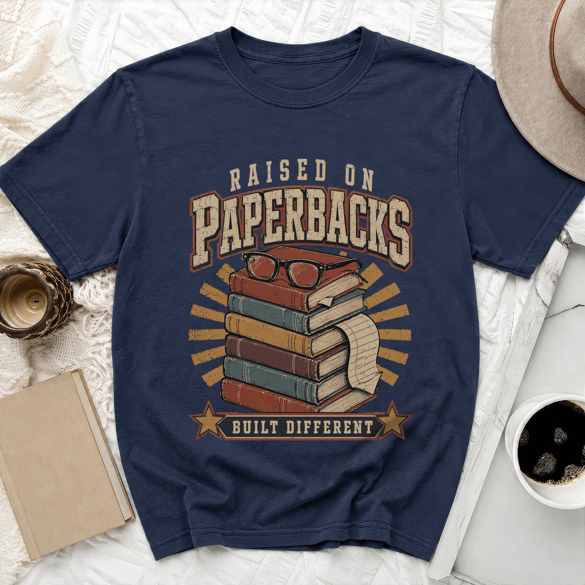 Navy t-shirt with graphic of stacked books, glasses, and text "Raised on Paperbacks Built Different".