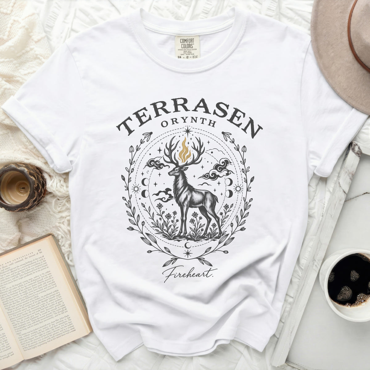 A white t-shirt featuring a detailed graphic of a stag surrounded by floral and celestial elements, with the text Terrasen and Fireheart.
