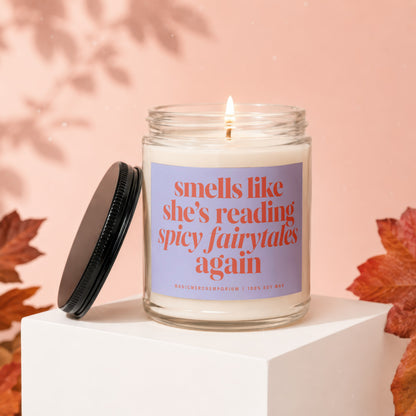 Candle with "smells like she's reading spicy fairytales again" text, lit flame, and fall leaves.