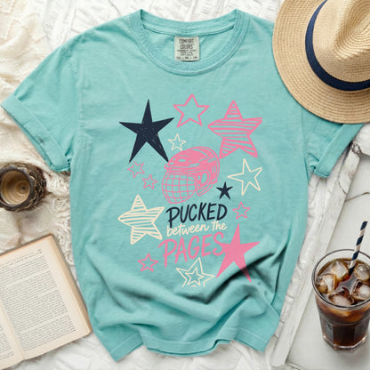Teal t-shirt with hockey puck and stars graphic, reading "Pucked between the Pages."