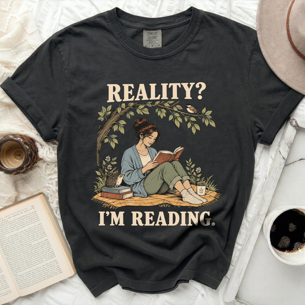 T-shirt with graphic of woman reading under a tree with text "REALITY? I'M READING."