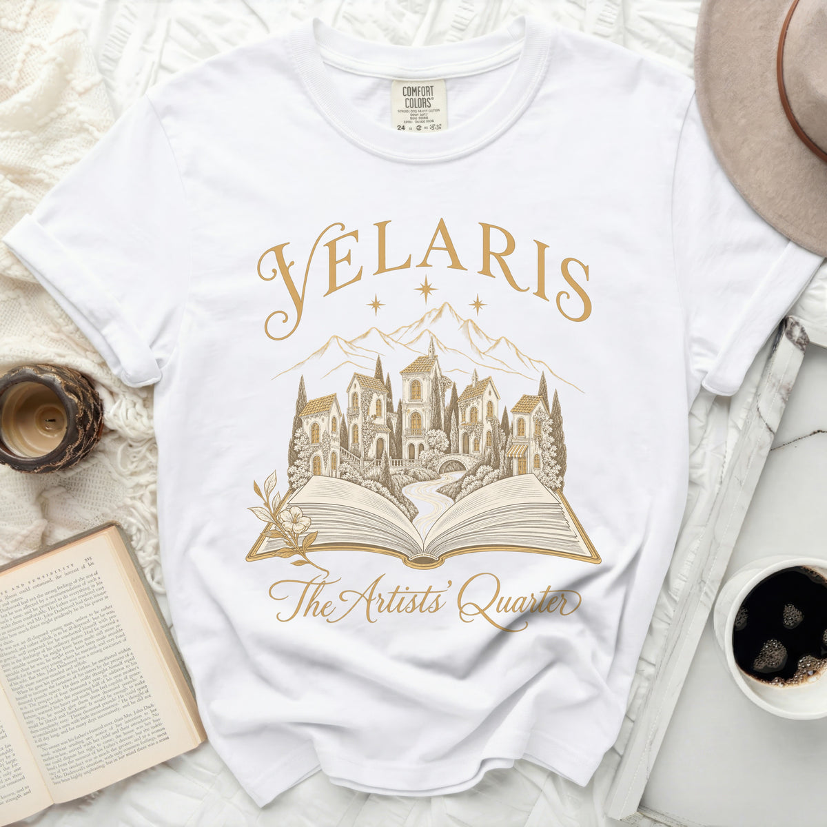 White t-shirt with gold text "Velaris The Artists' Quarter" over an open book design.