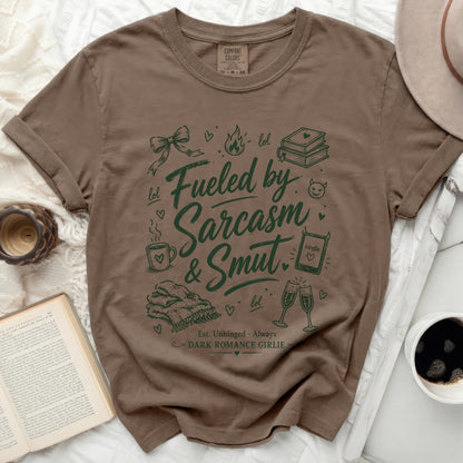 Brown t-shirt with "Fueled by Sarcasm & Smut" graphic and book, coffee, and champagne illustrations.