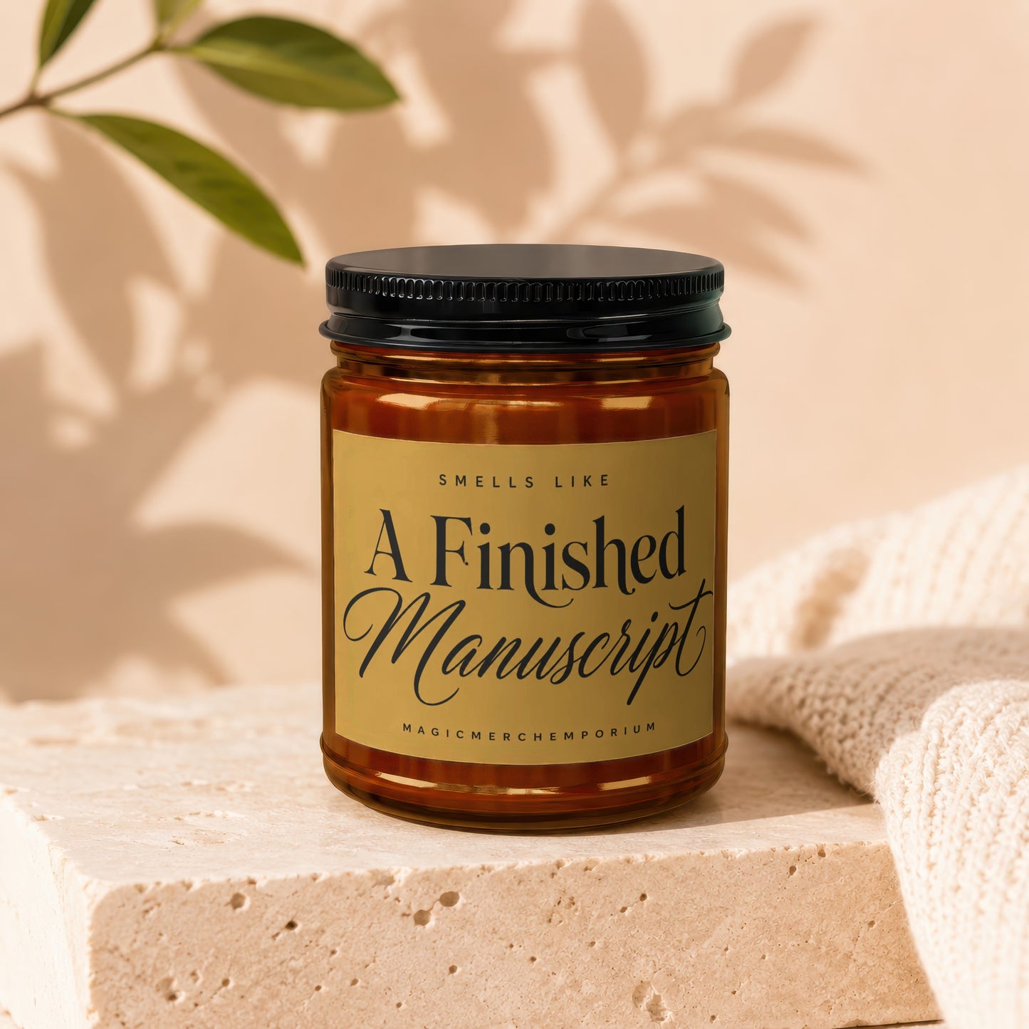 Candle with gold label reading "Smells Like A Finished Manuscript" and "MagicMerchEmporium."