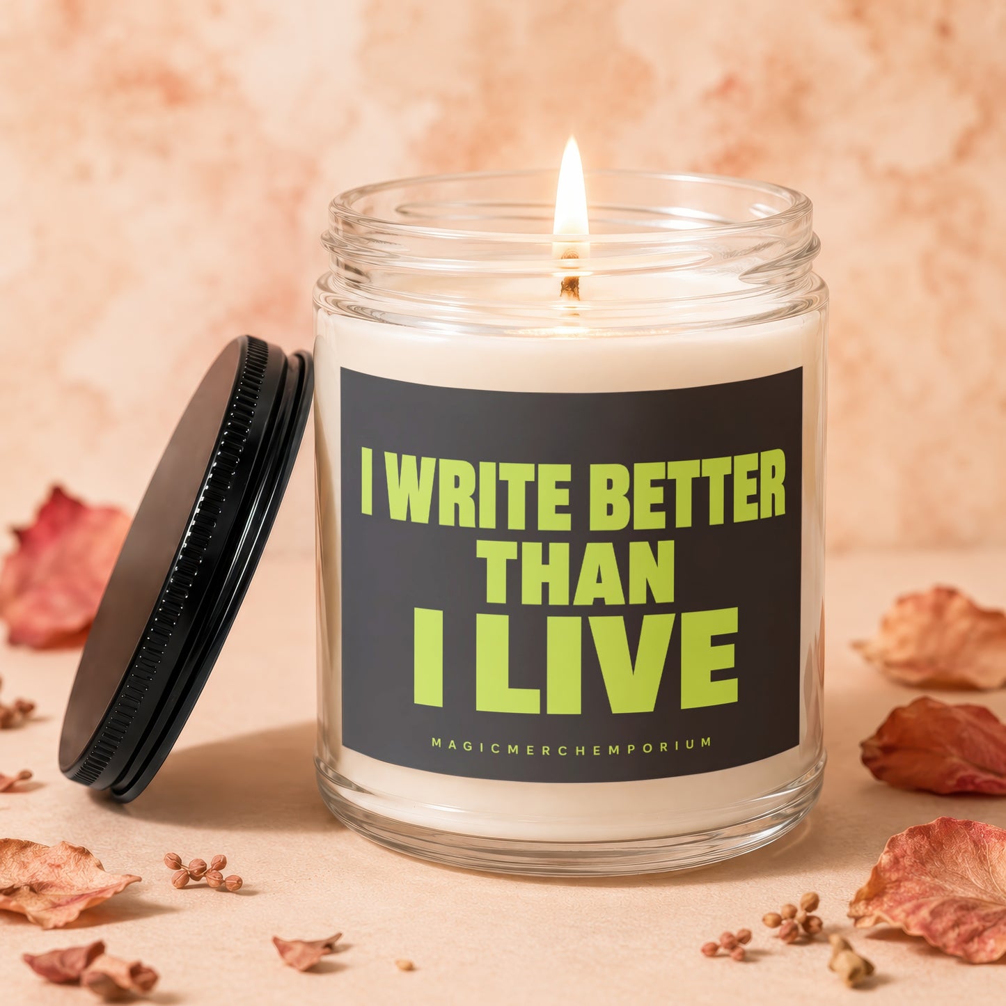 Lit glass candle with a black lid, featuring text "I WRITE BETTER THAN I LIVE".