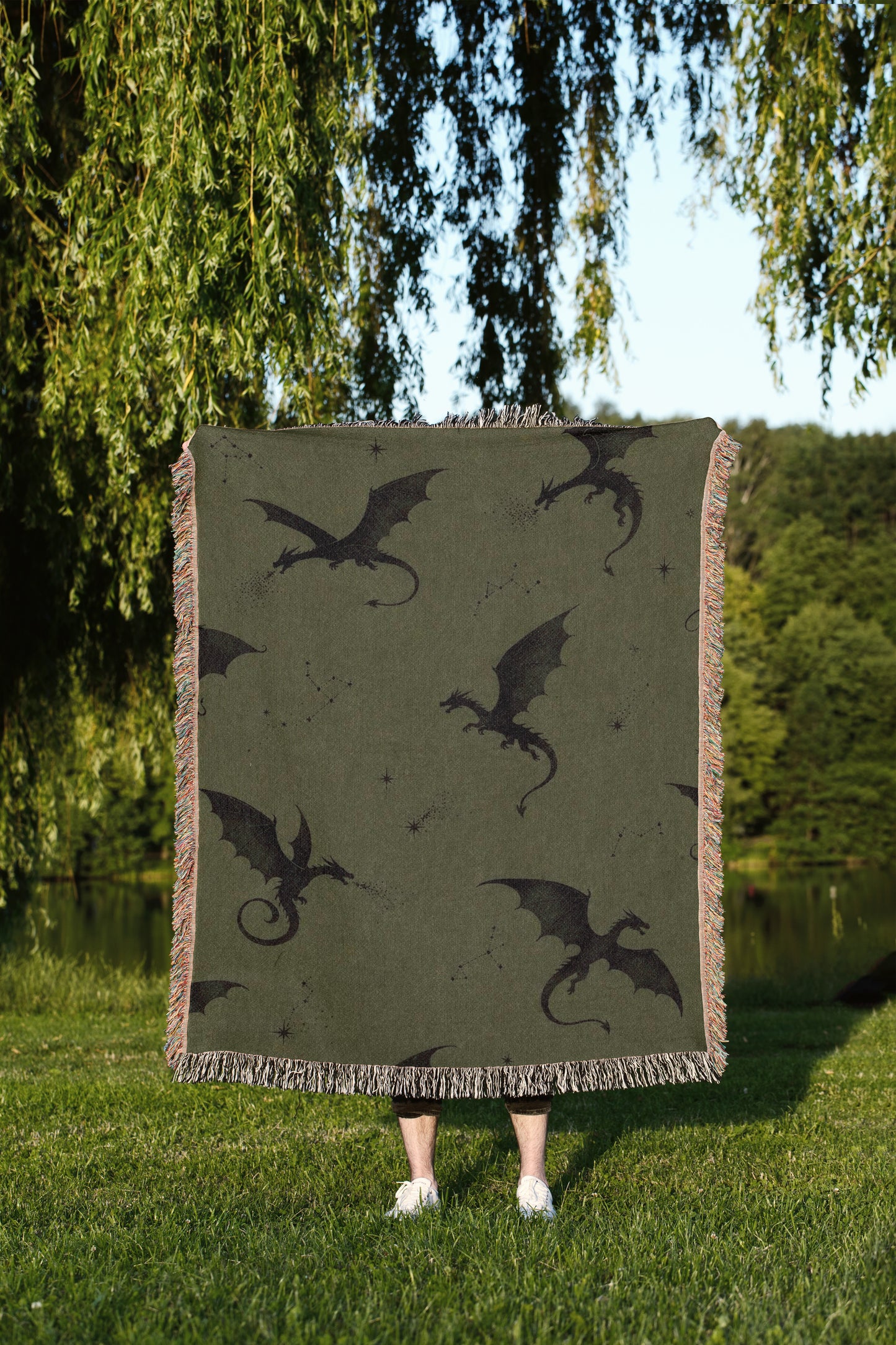 A person is standing in a grassy area, holding a large square blanket with a dragon design on it.