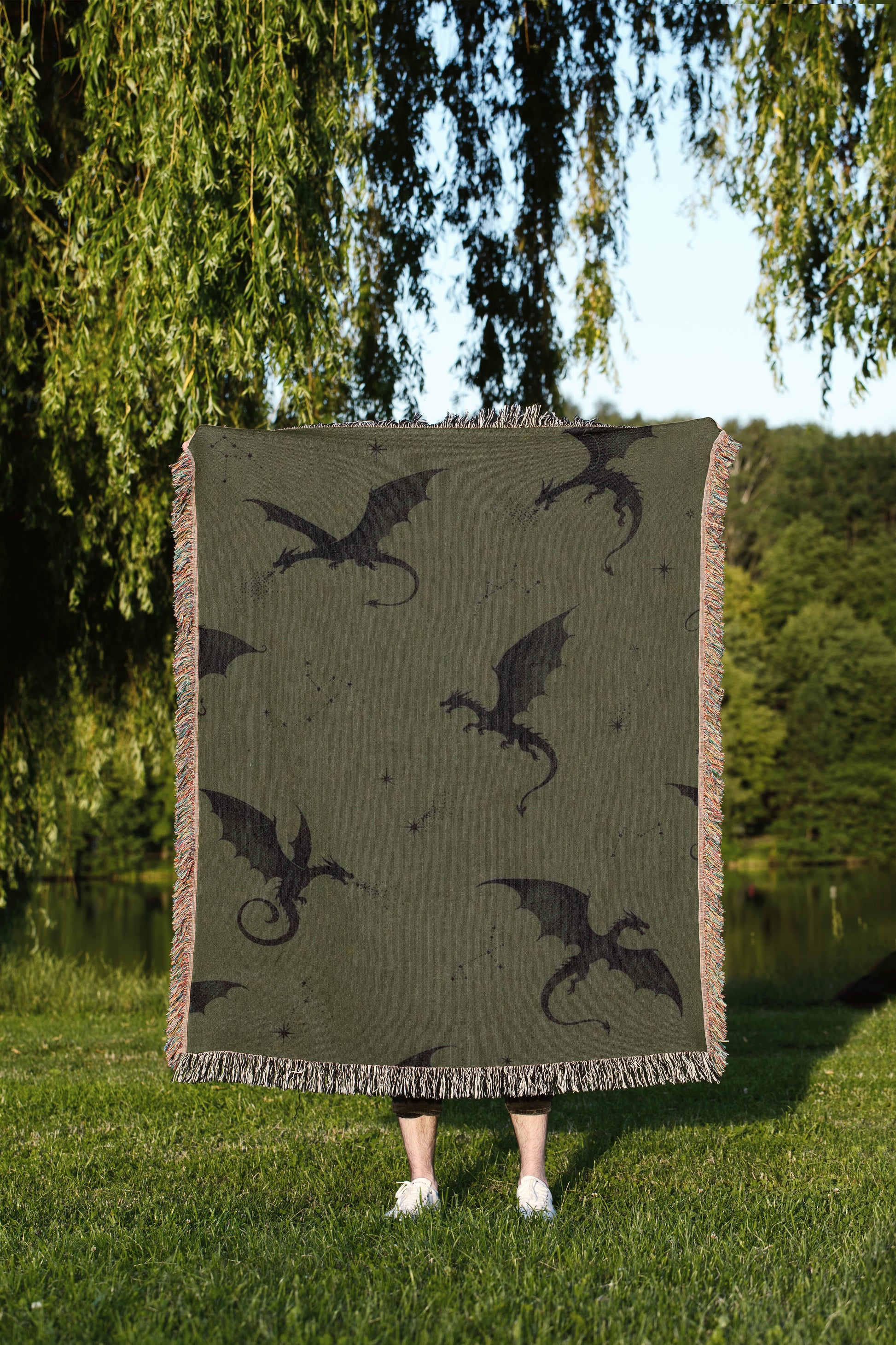 A person is standing in a grassy area, holding a large square blanket with a dragon design on it.