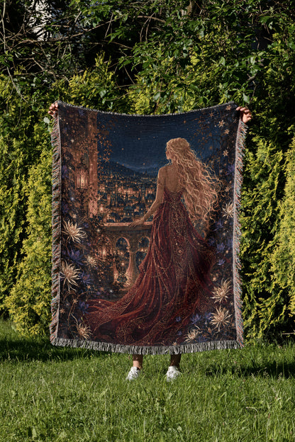 A person is holding up a large tapestry depicting a woman with long, flowing hair and a red dress, standing in a lush, green garden with a cityscape in the background.