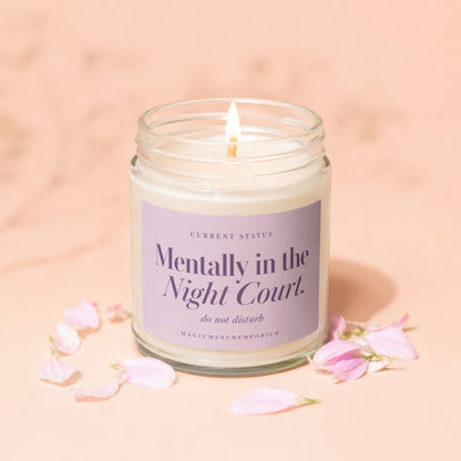 A lit candle in a glass jar with a purple label featuring text on a peach background.