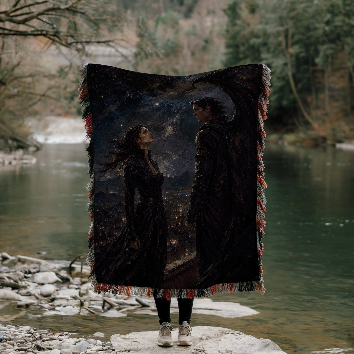 A person stands on a rock, holding a large blanket with a painting of a woman and a man on it, against a backdrop of a river and trees.