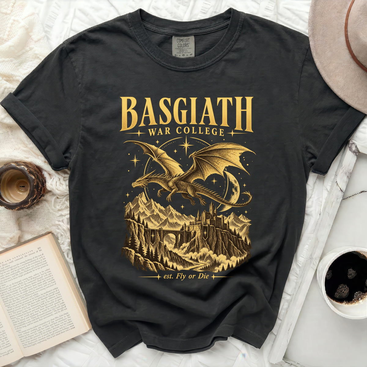 Dark t-shirt with gold graphic of a dragon over mountains and castle, "BASGIATH WAR COLLEGE" and "est. Fly or Die".
