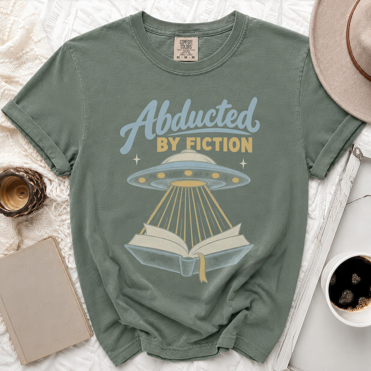 T-shirt with "Abducted by Fiction" text, UFO, and open book graphic.