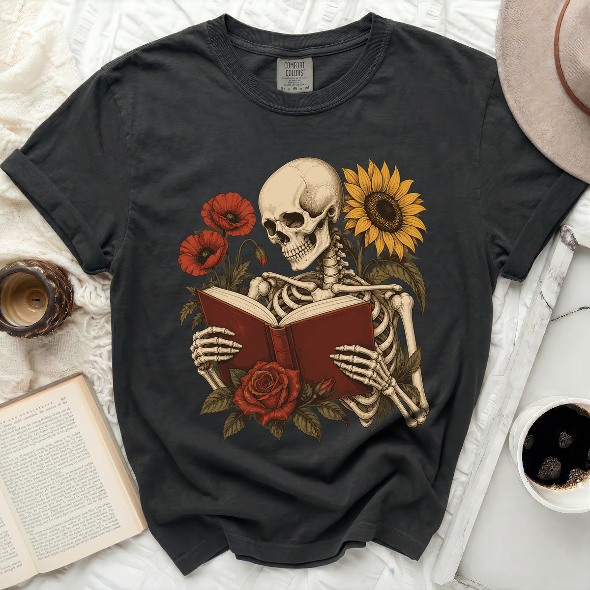 Skeleton reading a book surrounded by flowers and a sunflower.