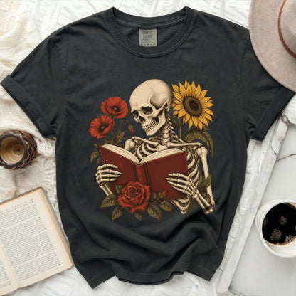 Skeleton reading a book surrounded by flowers and a sunflower.