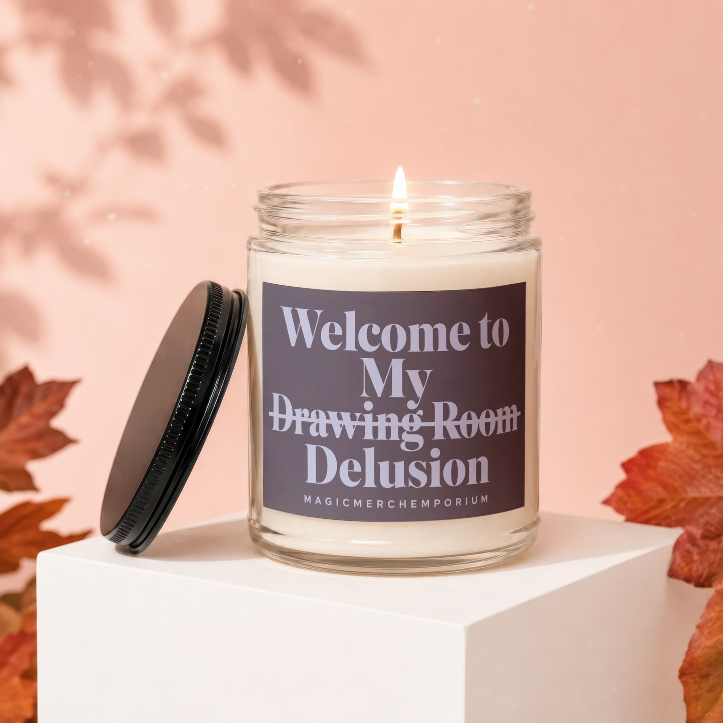 Candle with label "Welcome to My Drawing Room Delusion" on white block.