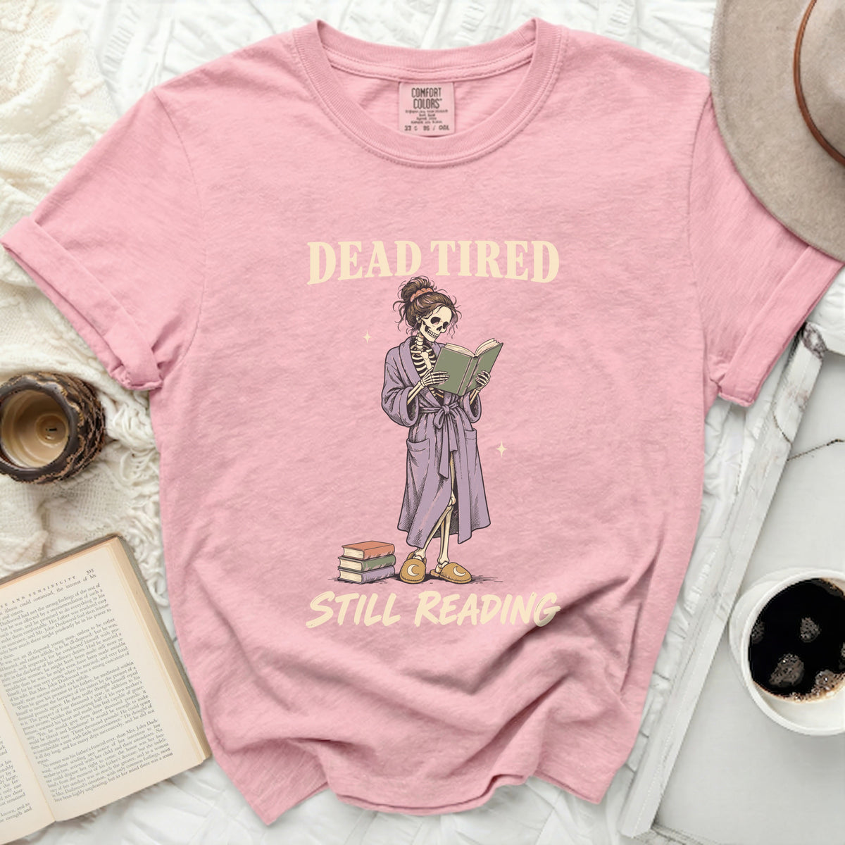 Pink t-shirt with skeleton reading book and text "DEAD TIRED STILL READING".